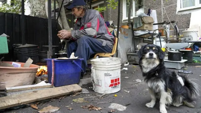 Un homme est assis près d'un poêle de fortune pour se réchauffer 
