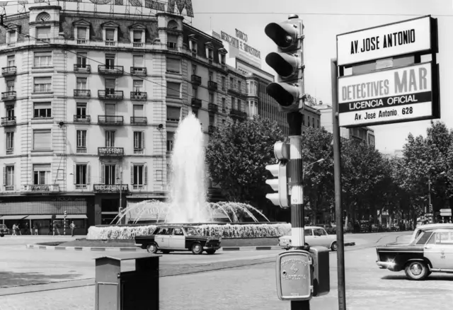 Barcelona a hatvanas évek végén, egy körforgalom látható autókkal, a középen egy szökőkút középen felszökő nagy vízsugárral és kisebb vízsugarakkal. 