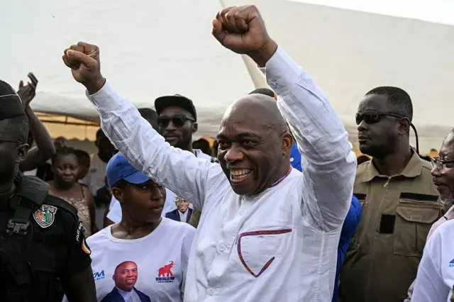 Le candidat indépendant ivoirien à la présidentielle, Ahoua Don Mello (au centre), serre les poings à son arrivée à son meeting de campagne à Port-Bouët, à Abidjan, le 15 octobre 2025. 