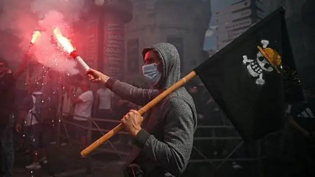 Seorang pengunjuk rasa memegang suar asap dan mengibarkan bendera bajak laut 