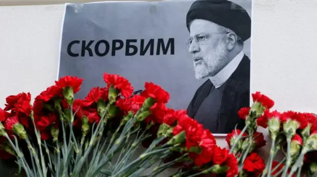 صورة الرئيس الإيراني إبراهيم رئيسي وأمامها مجموعة من الورود