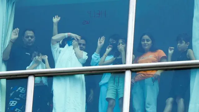 Young and old migrants in the Decápolis hotel stand at a window and try to catch the attention of those outside