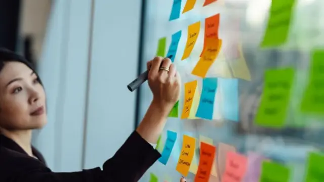 Une femme écrit sur des post-it collés à une vitre