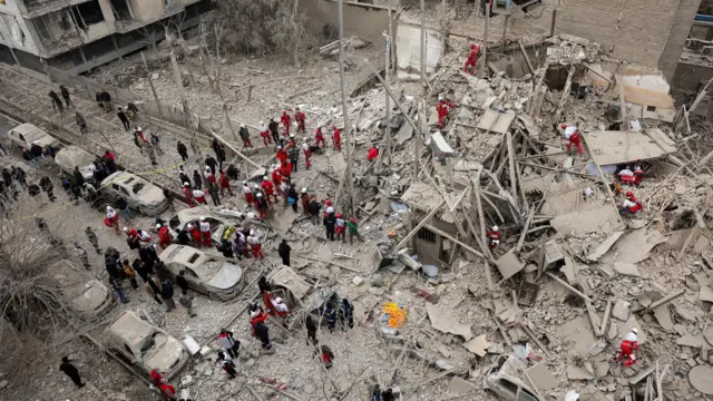 Emergency personnel, in red overalls, work in the rubble after a residential building was hit by an airstrike in Tehran, Iran
