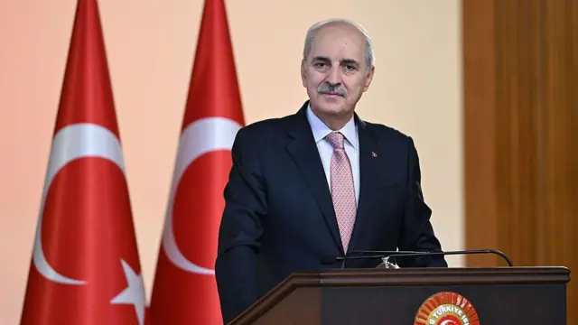 Numan Kurtulmuş arkasında iki türk bayrağı ile TBMM kürsüsünde kameraya bakıyor