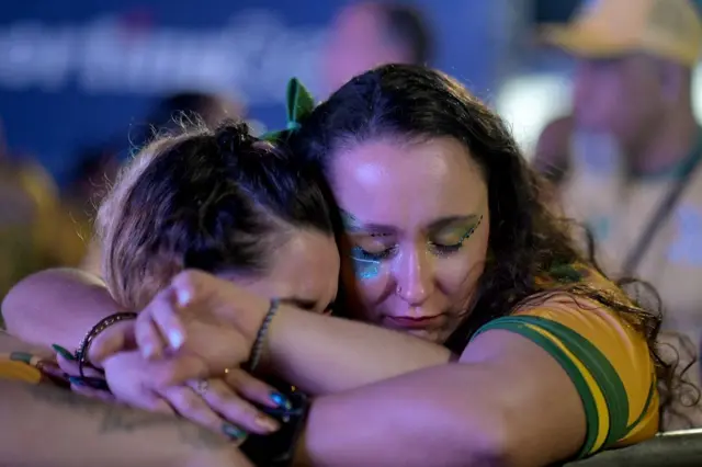 Duas mulheres abraçadas usando roupas do Brasil