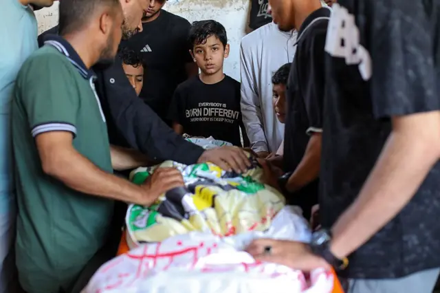 فلسطينيون يشاركون في مراسم تشييع جثمان عبد الحميد جروان، الذي قُتل في غارة إسرائيلية استهدفت مخيم النصيرات للاجئين وسط قطاع غزة، رغم سريان وقف إطلاق النار، ويظهر في الصورة جثمان طفل مغظى بأقمشةـ ويقف حوله مجموعة من الرجال وثلاثة أطفال.