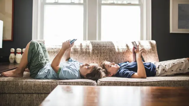 Duas crianças loiras olhando para seus telefones. Foto encenada por modelos.