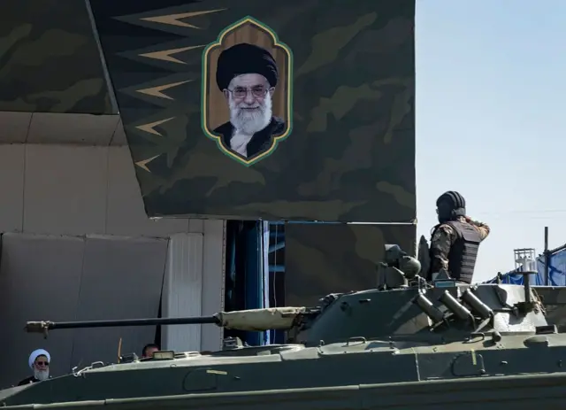 يؤدي جندي إيراني التحية العسكرية أثناء نقله على متن دبابة عسكرية أمام صورة المرشد الأعلى الإيراني، آية الله علي خامنئي، خلال عرض عسكري بمناسبة ذكرى يوم الجيش 2025
