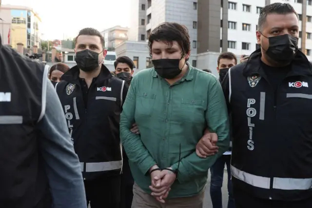 Mehmet Aydın yeşil gömlekli, elleri plastik kelepçeli halde polislerin arasındayken. 