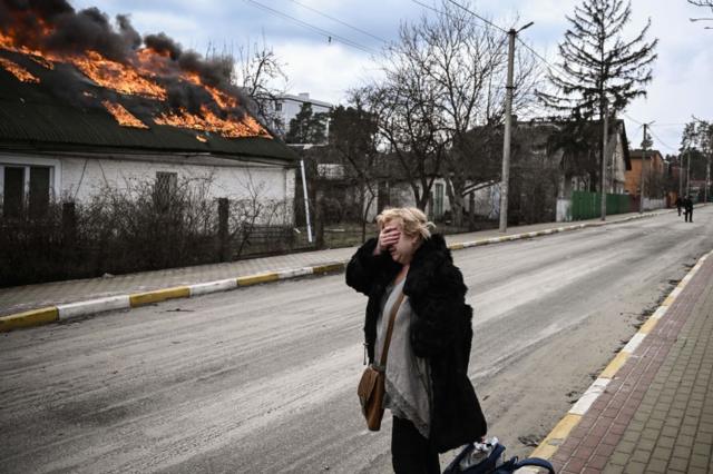 Uma mulher cobre o rosto com a mão enquanto está em frente a uma casa em chamas em Irpin, nos arredores de Kiev, 4 de março de 2022