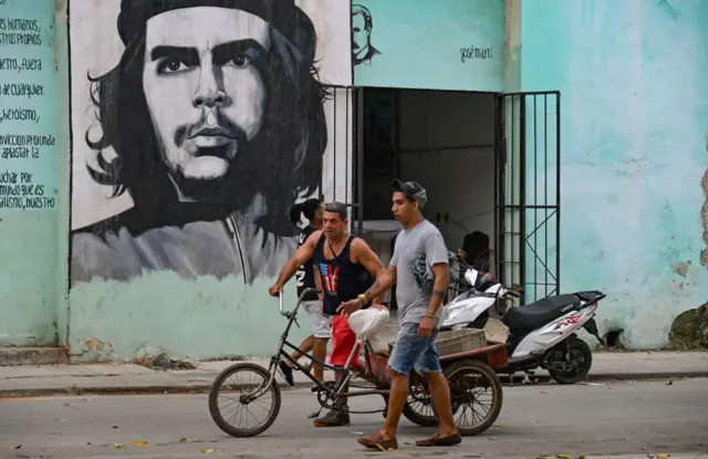 Dos personas empujan un triciclo bajo un retrato del "Che" Guevara en una calle de La Habana. 