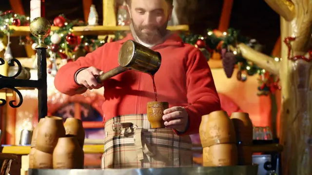 Mężczyzna przygotowuje grzane wino dla odwiedzających na stoisku podczas otwarcia corocznego jarmarku bożonarodzeniowego na Breitscheidplatz w Berlinie, 24 listopada 2025 roku.