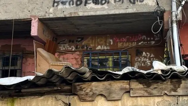 Boyasız binanın duvarında yazılar bulunuyor. Bir yazıda Allah korusun yazıyor.