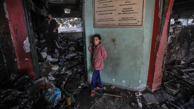 طفلة تقف بينما يظهر الدمار الذي سببته الغارة الإسرائيلية على مدرسة تؤوي نازحين في غزة