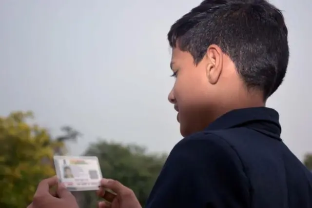 ஆதார் கார்டை பார்க்கும் சிறுவனின் புகைப்படம்