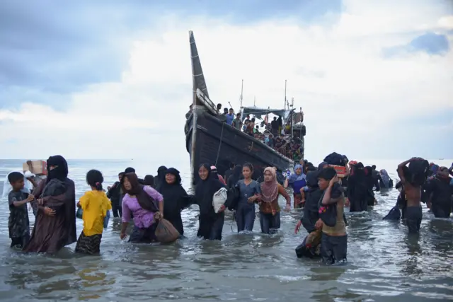 Muslim Rohingya berjalan melewati perairan setelah mereka diizinkan sementara oleh penduduk setempat untuk mendarat di pantai Ulee Madon, Aceh Utara, Indonesia, 16 November 2023.