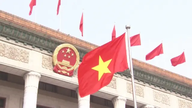 中国官方欢迎苏林仪式上，在北京人民大会堂外，一面越南国旗（右）在中国国徽（左）前飘扬（中国中央电视台片段截屏 15/4/2026）