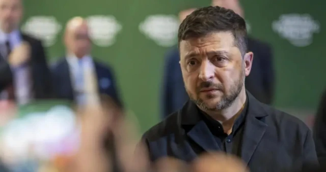 Zelenskiy gazetecilerin sorularını dinliyor, Üzerinde kravatsız bir siyah takım var.