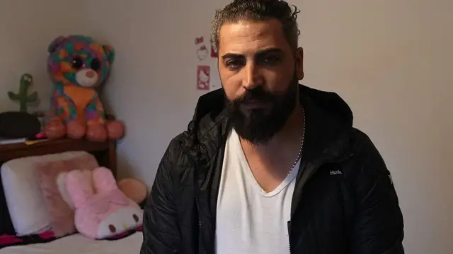 Oday al-Fayoume seated on his son Wadea's bed which is full of teddies