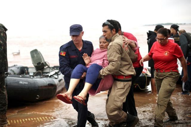 Mulher sendo carregada no colo em meio à enchente