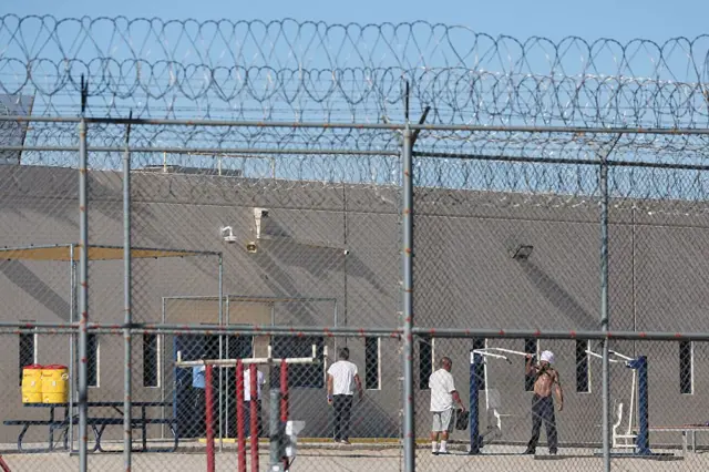 A través de las verjas y el alambre de concertina se ve a varios detenidos en el patio del centro de procesamiento del ICE en Adelanto, California, Estados Unidos, el 11 de julio de 2025. (Foto: PATRICK T. FALLON/AFP vía Getty Images)