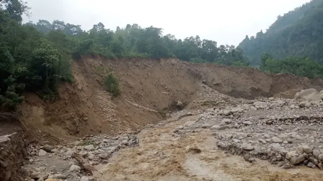 Landslide area with exposed soil, rocks, and surrounding forested hills.