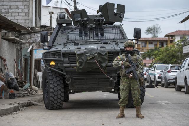 Un soldado armado delante de un vehículo miliar vigila en una calle de Ecuador