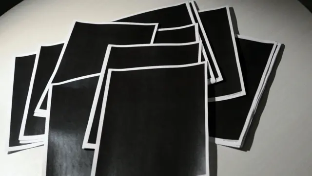 Decenas de páginas copletamente tachadas en negro yacen sobre una mesa.