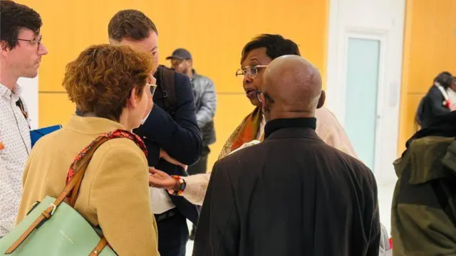 Abagore n'abagabo bo ku ruhande rwagiriza Charles Onana barimo baganira mu kirongozi c'inzu bakoze uruziga, umugore umwe akoze ikimenyetso n'ikiganza