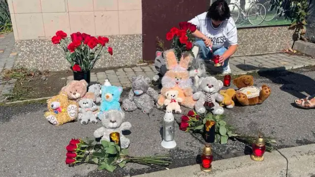 Меморіал вбитим хлопцям - іграшки, квіти та свічки, жінка запалює лампадку