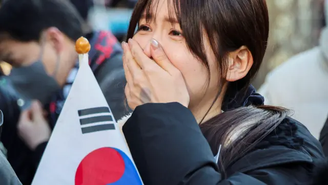 žena drži zastavu Južne Koreje i u neizvesnosti čeka vesti