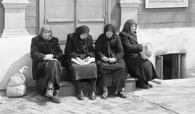 Чорно-біле фото чотирьох старших жінок, вони сидять на сходинці, на головах у них хустки