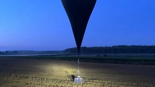 На фото пограничной службы Литвы метеозонд, похожий на небольшой воздушный шар, только вместо гондолы - упакованный в полиэтилен ящик, предположительно с контрабандными сигаретами. Снимок сделан вечером на поле и на фоне темнеющего неба и опушки леса