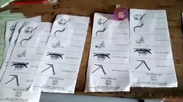 টেবিলের ওপর কয়েকটি ব্যালট পেপার রাখা। সেগুলোয় লাঙল, নৌকা, ধানের শীষ, কাচি ও হাতপাখা প্রতীক রয়েছে