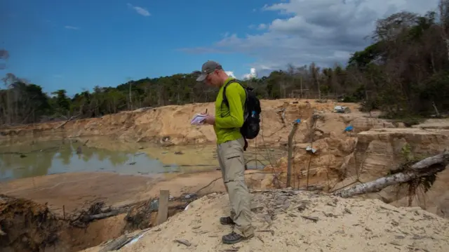 Phillips écrit quelque chose sur un bloc-notes dans un espace ouvert avec du sable et de l'eau.