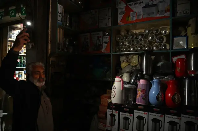 রাওয়ালপিন্ডি শহরে একটি দোকানে মোবাইল ফোনের টর্চ দিয়ে এক ক্রেতাকে পণ্য দেখাচ্ছেন দোকান মালিক