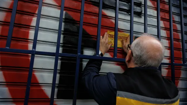 Agbalagba ọkunrin kan gbọwọ lori iwe alawọ olomi ọsan kan lara ti wọn lẹ mọ ara ilẹkun onirin