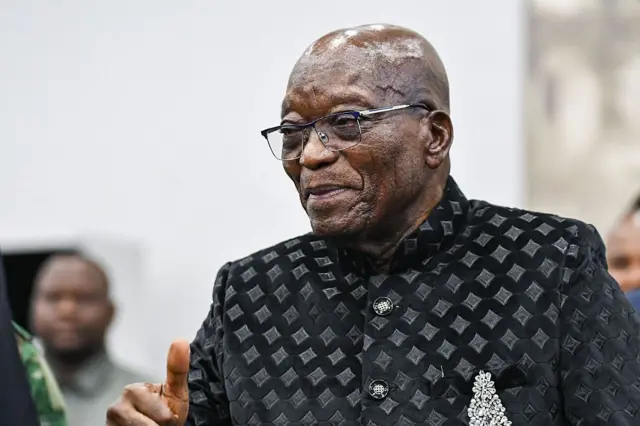 Jacob Zuma, ancien président d'Afrique du Sud, en costume noir avec des carrelés blancs, il porte des verres.