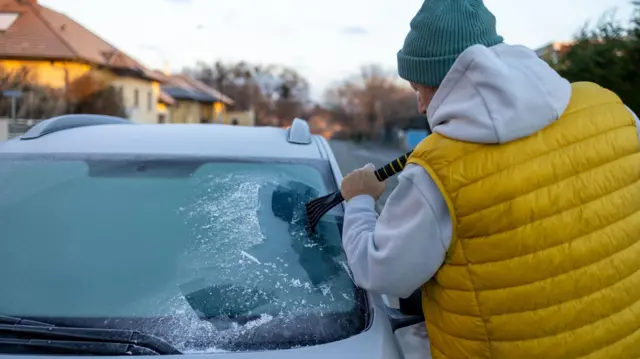 Un hombre raspa el hielo de su coche.