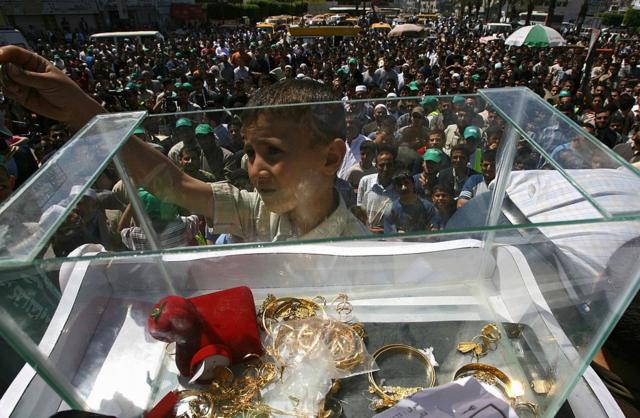 Một bé trai người Palestine bên cạnh một thùng đựng một số trang sức vàng quyên góp được tại Gaza