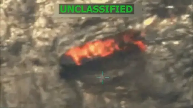Una imagen aérea de baja resolución muestra una lancha incendiada sobre el mar.
