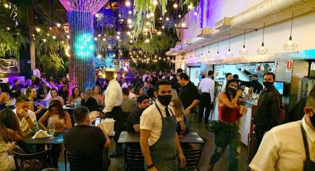 Restaurante lotado, com garçons usando máscara contra a covid