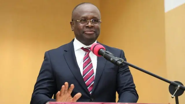 Omane Boamah sanye da baƙar ƙwat da farar riga a ciki ɗaure da jan ƙyalle yana jawabia a gaban makirfo