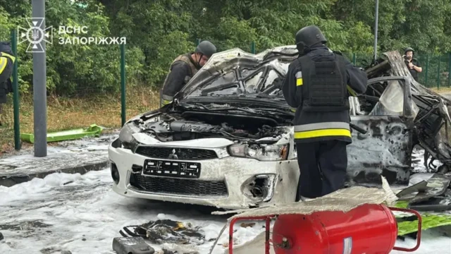 Двое спасателей исследуют сгоревший легковой автомобиль белого цвета