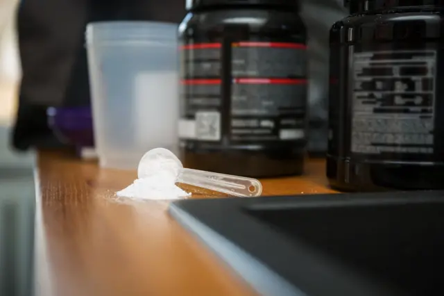Dos envases grandes de creatina en el fondo y una cucharada de creatina regada al frente