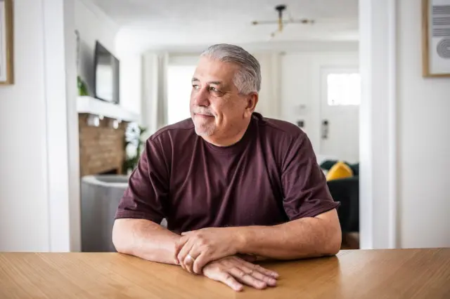 homem com cabelos brancos sentado com mãos sobre uma mesa