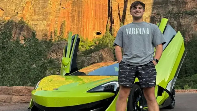Um homem branco, usando camiseta do Nirvana e bermuda, posa diante de um carro verde-limão com as portas abertas