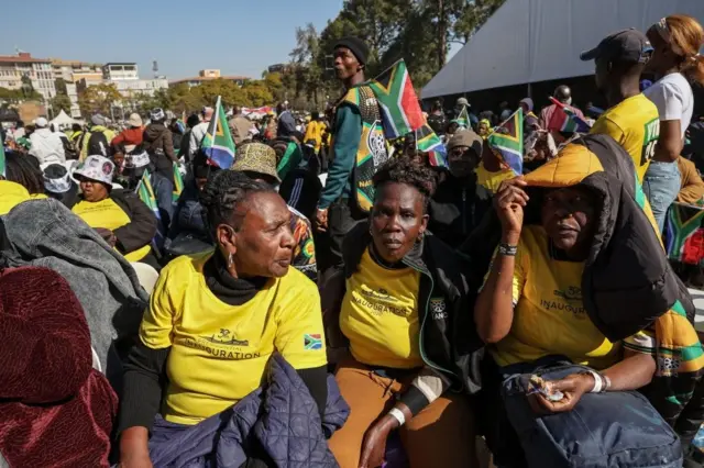 Des partisanes du président sud-africain Cyril Ramaphosa, habillées de T-shirts jaunes, sont assises lors d'un rrassemblent à l'investiture de Ramaphosa sur les pelouses sud des Union Buildings à Pretoria, le 19 juin 2024. 