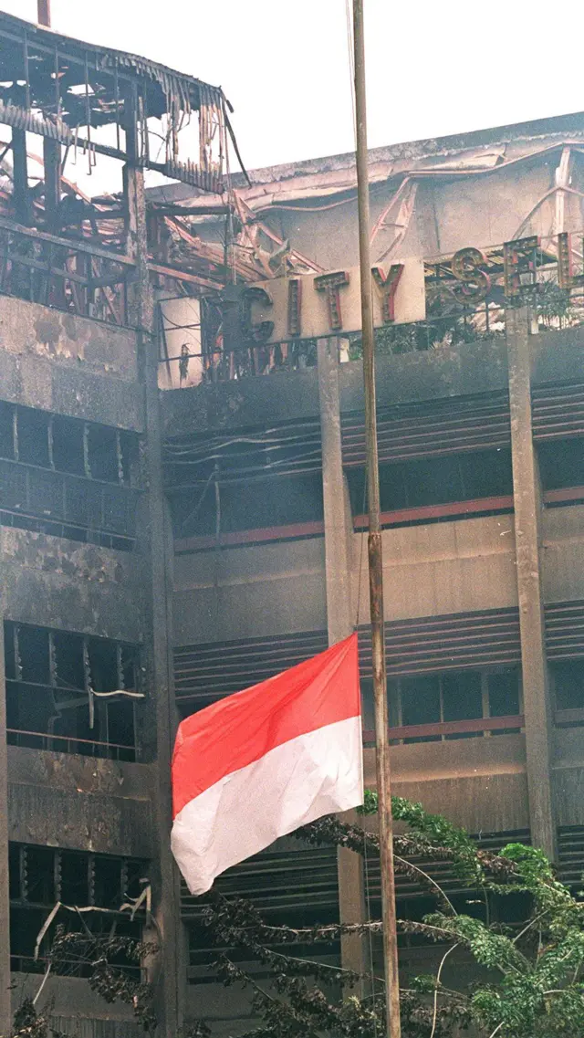Bendera Indonesia berkibar setengah tiang di depan sisa-sisa hotel yang terbakar di kawasan Pecinan Jakarta